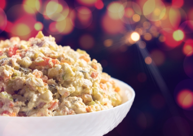 Olivier russian salad - a classic recipe with mayonnaise, an incredible taste, on a black background, with bokeh of sparklers for christmas and new year.